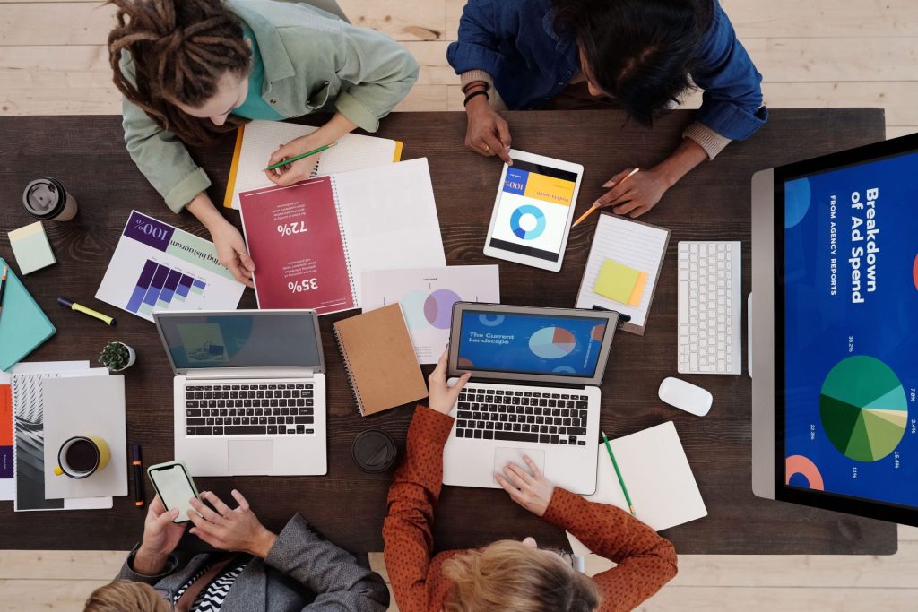 Ein vielfältiges Team arbeitet an einem Schreibtisch an Strategien für digitales Marketing und nutzt dabei Laptops und Tablets.