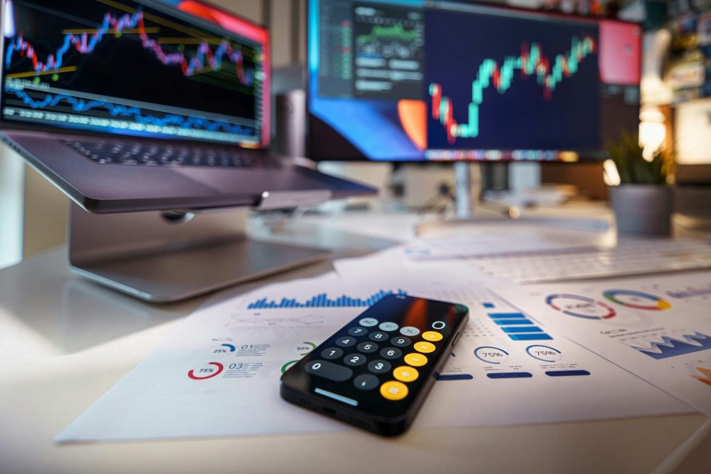 Smartphone-Taschenrechner auf dem Schreibtisch mit Finanzdiagrammen im Hintergrund